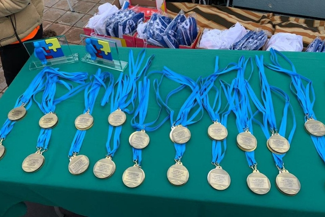 En una mesa apoyadas las medallas y premios de los participantes de la Carrera Azul organizada por la Asociación Mírame